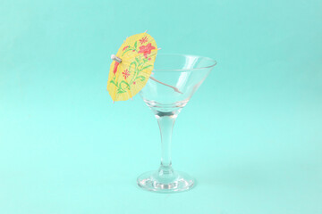 Empty cocktail glass with umbrella on blue background. Creative idea. Minimal party concept, layout