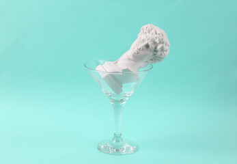 Plaster bust of David in cocktail glass on blue background. Fresh idea. Minimal party concept, creative layout