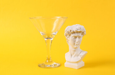 Plaster bust of David in cocktail glass on yellow background. Fresh idea. Minimal party concept, creative layout