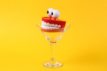 Toy jaw in cocktail glass on yellow background. Fresh idea. Minimal party concept, creative layout