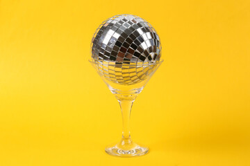 Cocktail glass with disco ball on yellow background. Creative idea. Minimal party concept, layout