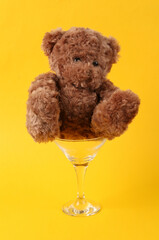 Teddy bear in cocktail glass on yellow background. Creative idea. Minimal party concept.