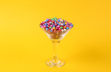 Colored balls in cocktail glass on yellow background. Fresh idea. Minimal party concept, creative layout