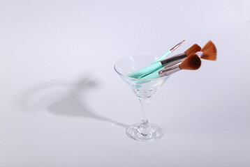 Makeup brushes in a cocktail glass on gray background. Minimal beauty layout