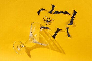 Cocktail glass with bats and a spider on yellow background. Halloween party