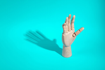 Wooden hand on a turquoise background with long shadow. Minimal layout