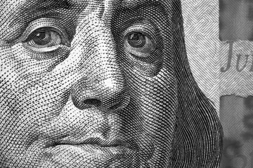 Black and white background or wallpaper about economy or finance. US dollar. Benjamin Franklin face close-up on a fragment of a 100 USD banknote. Reduced contrast. Macro
