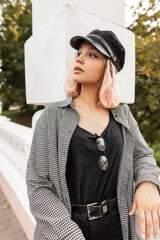 Beautiful teenager girl with pink hair in fashionable clothes with a shirt and a vintage cap is walking on the street