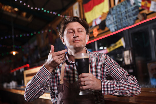 Mature male brewer smelling aromatic freshly brewed beer at his pub