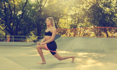 Beautiful young fit woman doing morning exercise with fitness rubber bands outdoors.