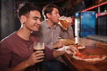 Happy young man enjoying beer and pizza with his friend at the bar