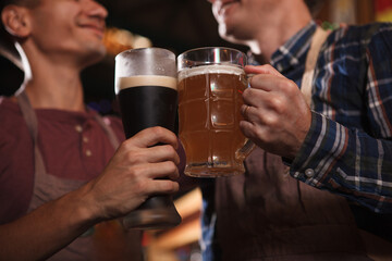 Cropped close up of brewers clinking beer glasses