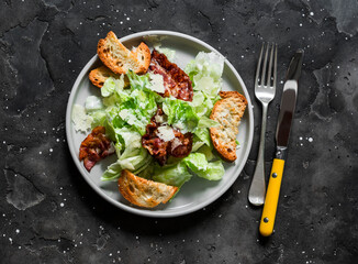 Caesar salad with bacon on a dark background, top view. Delicious brunch, appetizer, tapas
