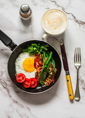 Delicious breakfast in a frying pan - fried egg, bacon, asparagus, tomatoes on a light background, top view