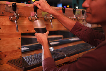 Cropped close up of a bartender pouring beer from the tap into glass