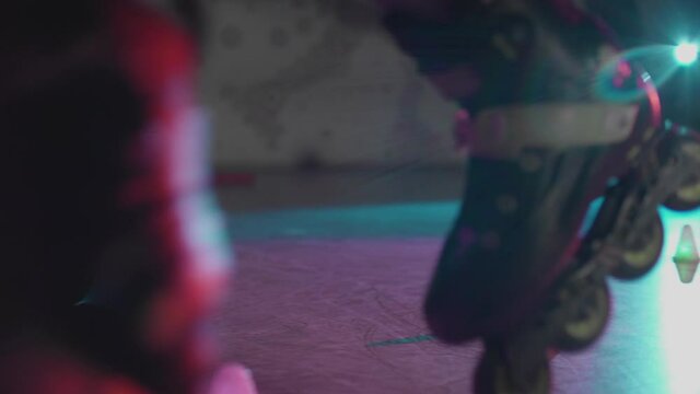 Close-up of teenager legs roller skating around obstacles in slow motion. Millennial showing trick freeskating in dark studio with colourful lights. Concept of lifestyle, activity, nightlife.
