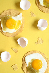 Broken fried eggs next to shells, yellow background