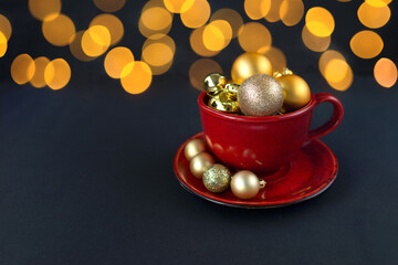 Obraz na płótnie Canvas Red cup with golden Christmas balls inside, on a black background with golden bokeh lights 