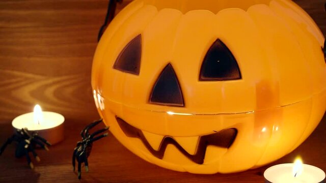 Glowing plastic pumpkin toy as a decoration of a room for Halloween celebrate. Halloween toy and burning candles on a wooden desk. Video 4k resolution