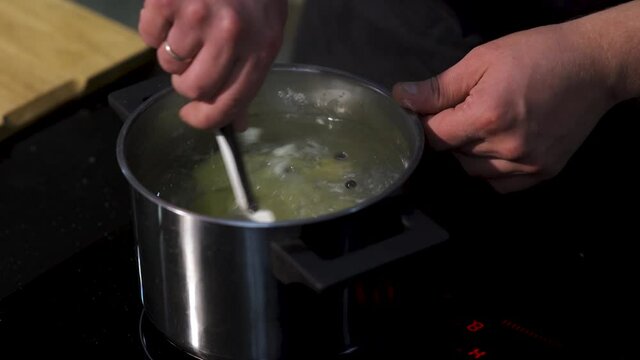 Close up of preparing soup, broth with potato and black pepper grains. Art. Chef hands stirring soup with a kitchen spatula.