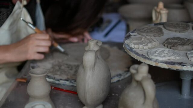  Traditional pottery. A close-up shot of making a clay plate. A close-up shot of female hands working on a clay plate. On the table are several clay pots waiting to be further processed