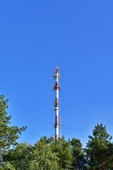 Tower with radio and telecommunication devices over green forest against blue sky