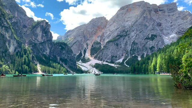 Panoramic shot of Lake Braies (Pragser Wildsee) and mountains and trees of the Dolomites in South Tyrol, Italy during summer with clouds and canoe