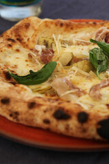 Delicious traditional Italian pizza with artichokes, prosciutto (ham), mozzarella, white sauce and basil baked in a wood-fired oven in Milan, Lombardy, Italy. European fast food and traditional dishes