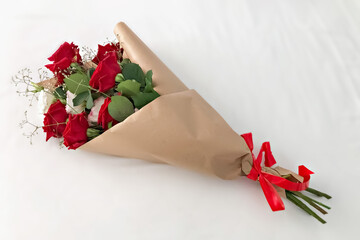 Red roses wrapped in brown kraft paper and tied with a red ribbon on a white background.