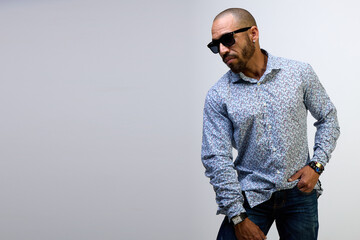 Portrait of a cool Latino man with a beard, wearing black sunglasses and a shirt on a white background
