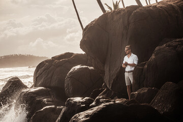 Fototapeta Mężczyzna elegancko ubrany stojący na skałach na tle oceanu i wzburzonych fal. obraz