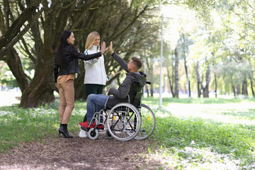 Disabled man in wheelchair giving five to female friends in park