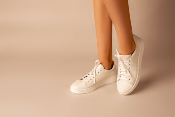 White sneakers shoes and girl’s legs on nude background - casual footwear