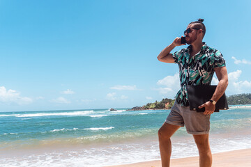 Mężczyzna z laptopem i telefonem na tle tropikalnego wybrzeża