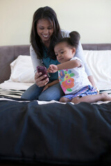 Fototapeta premium Mother showing daughter mobile phone on bed