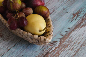 Still life with fruits pears and plums lie on a wicker plate in the form of a boat which stands on boards in the style of Provence against the wall