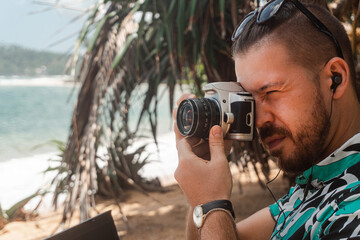 Młody mężczyzna, fotograf robiący zdjęcia na plaży podczas podróży. - obrazy, fototapety, plakaty