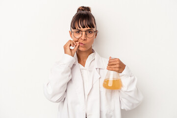 Young mixed race scientist woman holding a test tube isolated on white background  with fingers on lips keeping a secret.