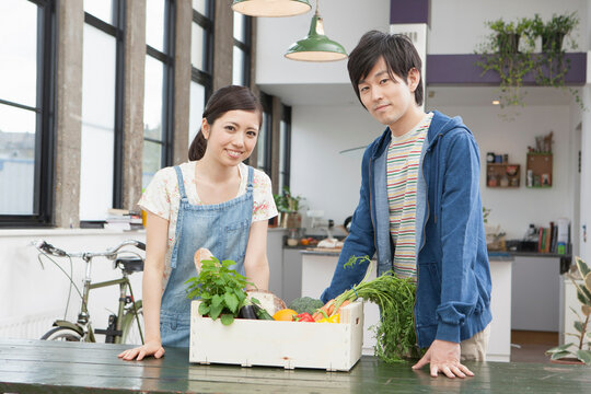 Portrait of young couple in kitchen with box of vegetables