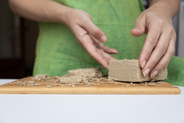 a woman holds a sunflower halva on a wooden board with sunflower seeds in her hands