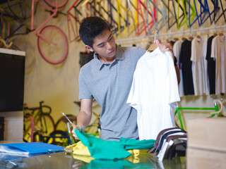Young man holding t shirts in bike shop