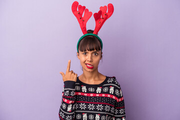 Young mixed race woman with reindeer hat celebrating Christmas isolated on purple background  showing a disappointment gesture with forefinger.