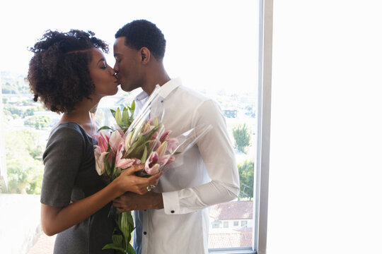 Young couple kissing, woman holding bouquet