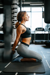 Young woman in sports clothes does yoga in the gym sitting on the floor stretching her back muscles. Concept of fitness and health.