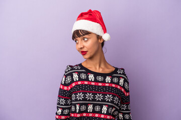 Young mixed race woman celebrating Christmas isolated on purple background  looks aside smiling, cheerful and pleasant.