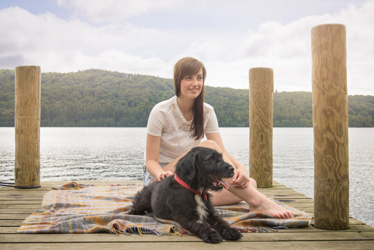 Young woman sitting with pet terrier at the end of a lakeside jetty
