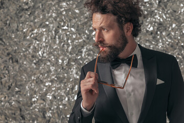 cool sexy man in black tuxedo looking to side while holding sunglasses