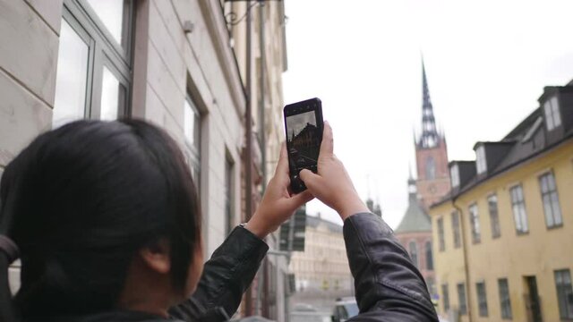 Asian woman standing and taking a picture around the town in Sweden, using smartphone taking a photo on street, beautiful town in sweden concept