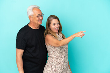 Middle age couple isolated on blue background presenting an idea while looking smiling towards