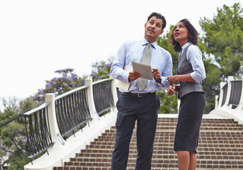 Business people standing in front of stairway holding digital tablet, looking up